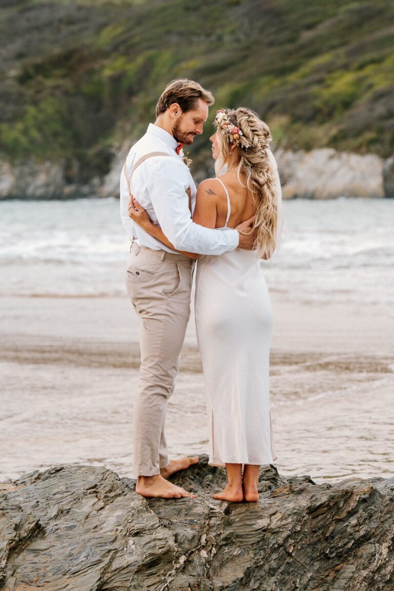 Couple standing on rock at beach elopement in cornwall