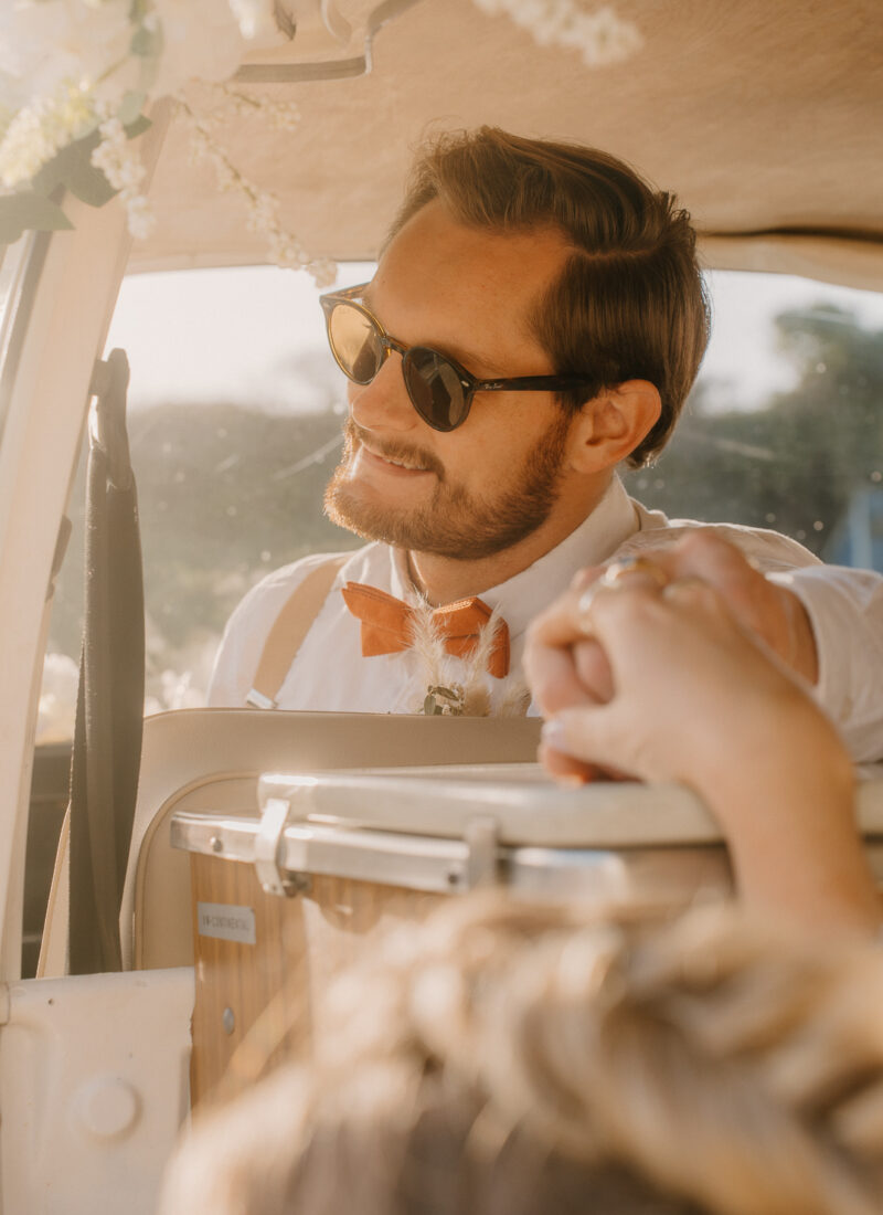 Shoot over brides head as holding hands with groom in a vintage VW camper with golden light coming in.