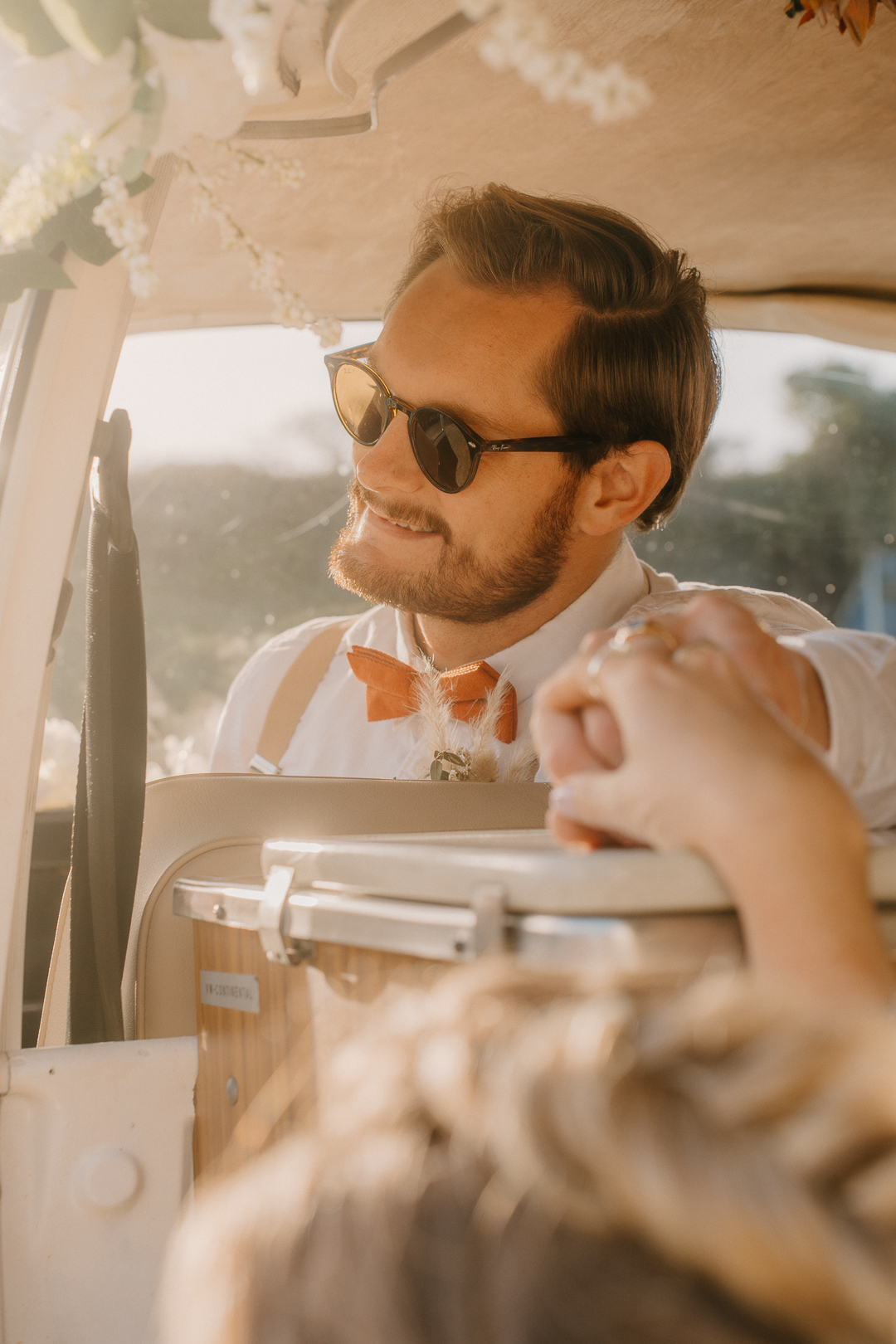 Shoot over brides head as holding hands with groom in a vintage VW camper with golden light coming in.