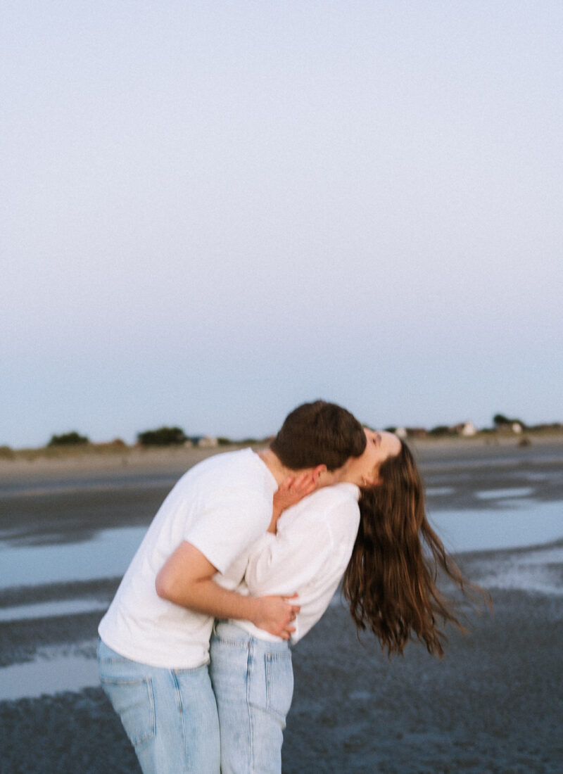 Couple in embrace at the beach during blue hour, her hair blowing in the wind.