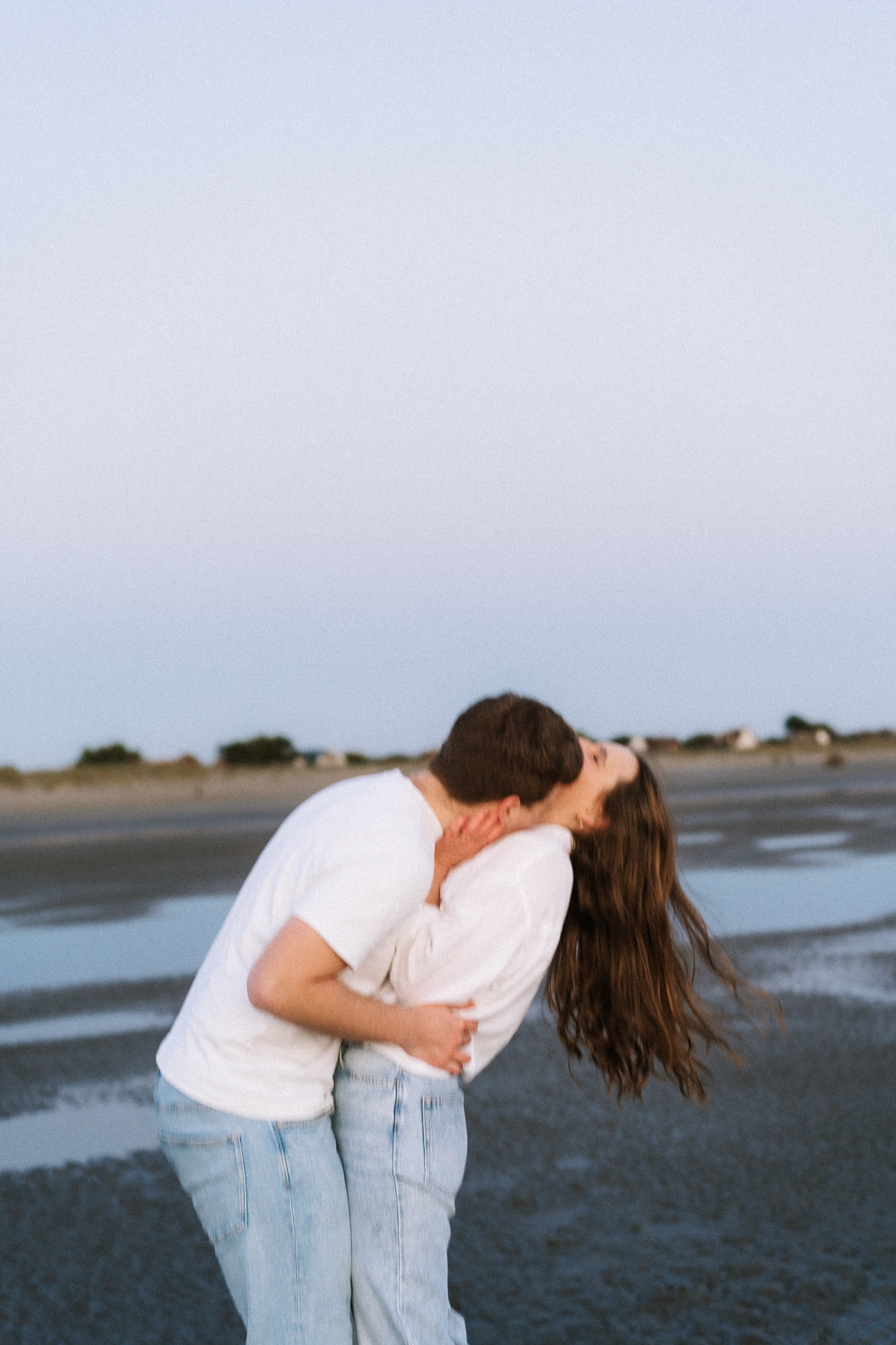 Couple in embrace at the beach during blue hour, her hair blowing in the wind.