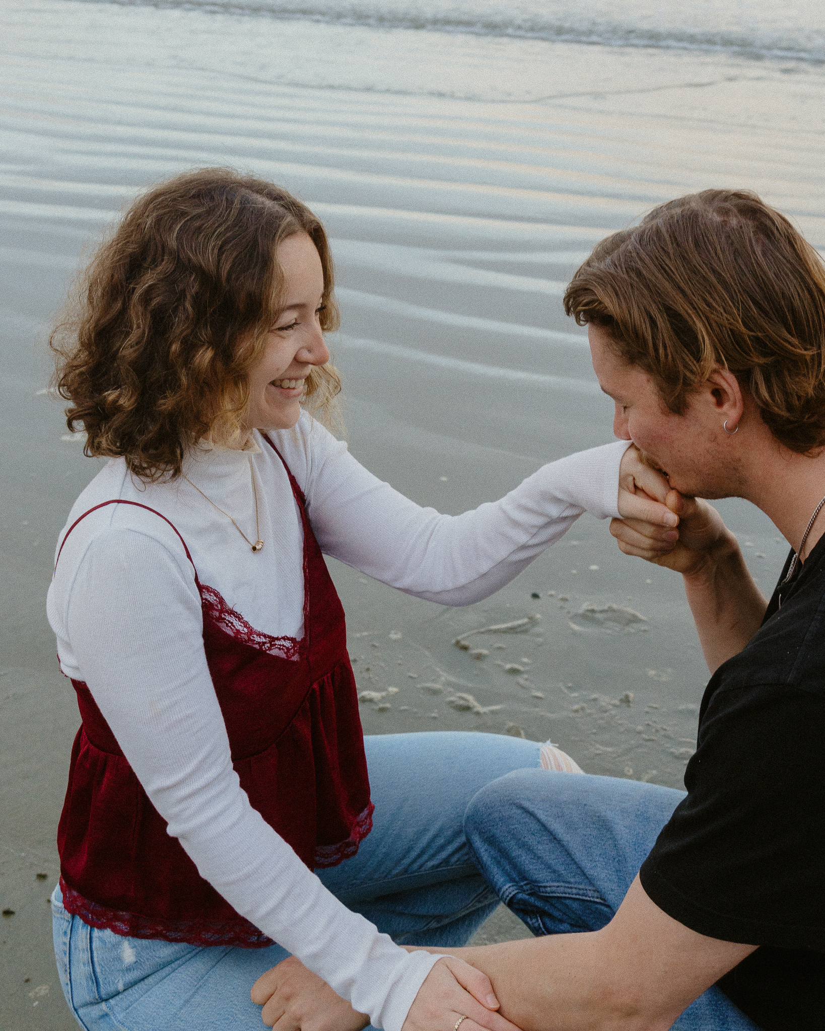 Couple crouching on Chesterman Beach in Tofino, he's holding and kissing her hand.