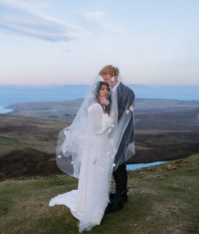 Bride and Groom standing on mountain top at sunset on the Isle of Skye on their wedding day.