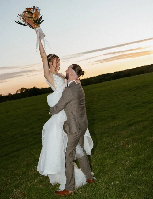 Groom holding bride up and spinning while bride throws bouquet up in the air.