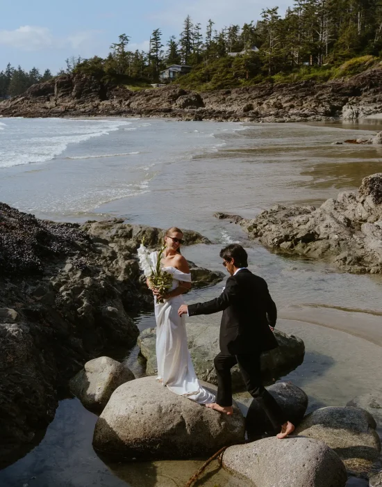 Groom jumping on rocks to get to bride in the rock pools at Chesterman Beach, Tofino.